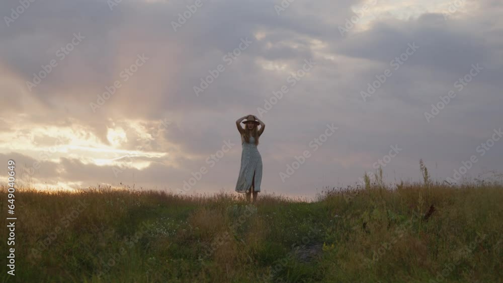 A young girl in a hat dances against the backdrop of a beautiful summer sunset and looks at the camera. Slow motion. A young girl in a hat dances against the backdrop of a beautiful summer sunset and looks at the camera. Slow motion.