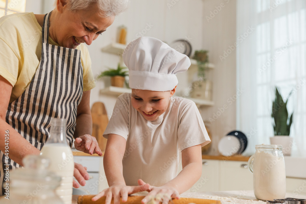 Happy family in kitchen. Grandmother and granddaughter child cook in kitchen together. Grandma teaching kid girl roll out dough bake cookies. Household teamwork helping family generations concept Happy family in kitchen. Grandmother and granddaughter child cook in kitchen together. Grandma teaching kid girl roll out dough bake cookies. Household teamwork helping family generations concept