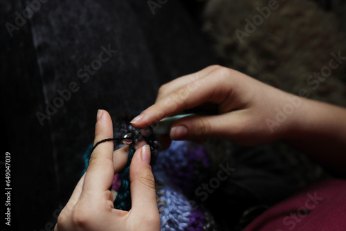 Skillful fingers of a young lady holding crochet hook and wool thread. Girls hands crocheting handmade jacket. Handcraft hobby  creating for kraft art or farmer fashion market. Selective focus