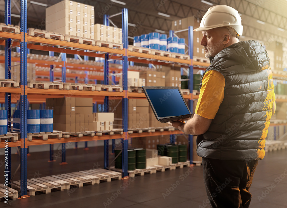 Man in warehouse. Logistics center employee. Worker with laptop in warehouse. Man inspects warehouse racks. Barrels and boxes are stored on pallets. Businessman with laptop in storage building Man in warehouse. Logistics center employee. Worker with laptop in warehouse. Man inspects warehouse racks. Barrels and boxes are stored on pallets. Businessman with laptop in storage building