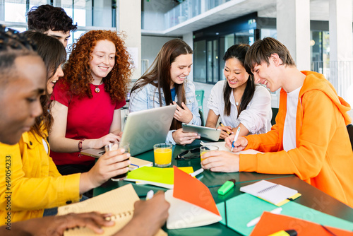 Young group of high school students studying together at cafeteria campus table. Diverse young people with books and laptops doing group study. Education and teamwork concept.