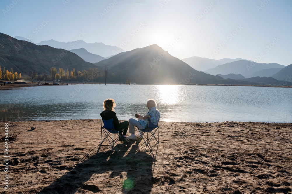 Senior man and his daughter relaxing together sitting outdoors near a lake in nature.