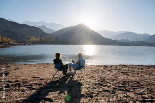 Senior man and his daughter relaxing together sitting outdoors near a lake in nature.