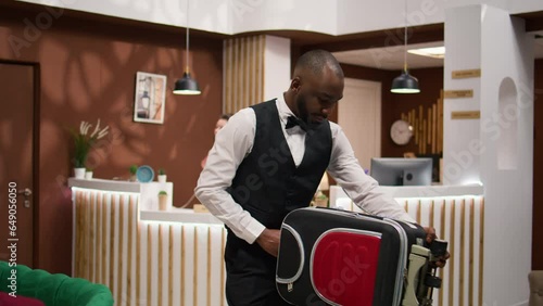 African american bellboy takes suitcases to help important guest with room accommodation, providing luxurious concierge services in hotel lobby. Employee wecoming and assisting businessmen. photo