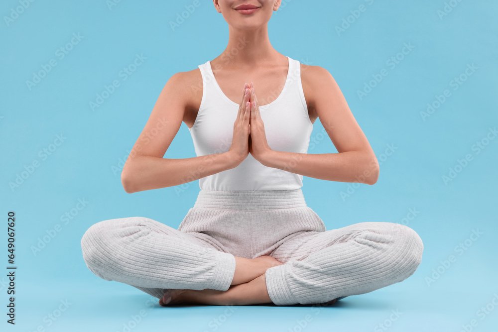 Woman practicing yoga on light blue background, closeup. Lotus pose Woman practicing yoga on light blue background, closeup. Lotus pose