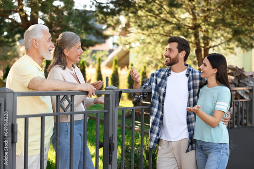 Friendly relationship with neighbours. Young family talking to elderly couple near fence outdoors photo
