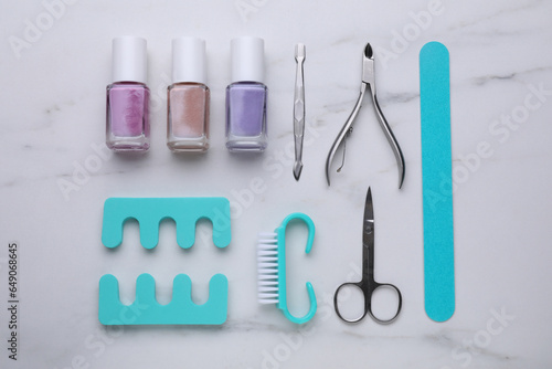 Set of pedicure tools on white marble table, flat lay