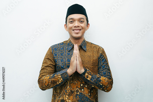 Portrait of an Asian Indonesian man in traditional Batik shirt placing his hands in front of his chest as a gesture of apology photo