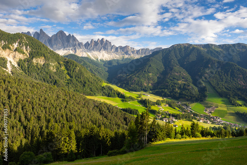Picturesque landscapes of alpine highland valley of Val di Funes located at foot of rocky mountains of Italian Dolomites with green meadows, dense forests and charming rustic houses on sunny day © JackF