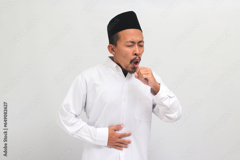 an Unwell young Indonesian man, wearing a songkok, peci, or kopiah, is coughing and sneezing, suffering from a cough, flu, and allergies, isolated on a white background an Unwell young Indonesian man, wearing a songkok, peci, or kopiah, is coughing and sneezing, suffering from a cough, flu, and allergies, isolated on a white background
