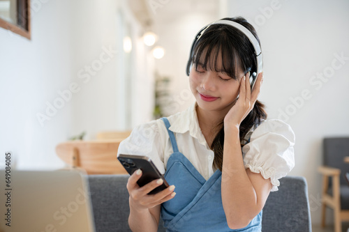 A happy Asian woman enjoys listening to music on her headphones while relaxing in a coffee shop.