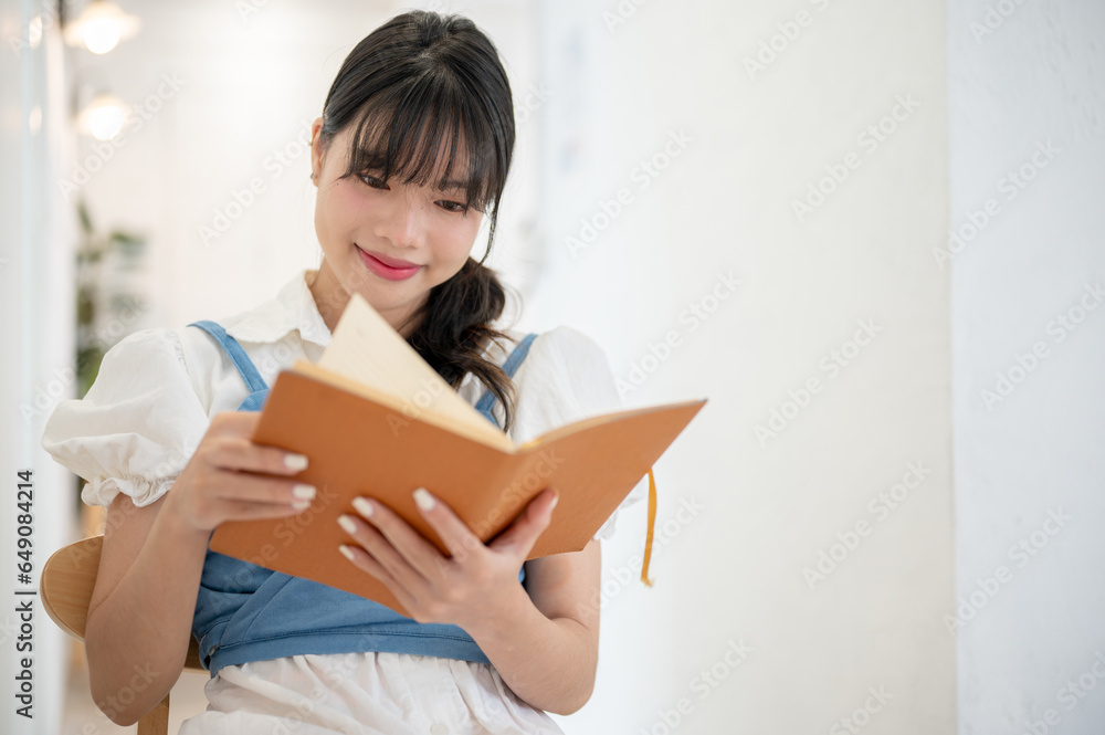 A beautiful and happy Asian woman enjoys reading a book while relaxing in a coffee shop. A beautiful and happy Asian woman enjoys reading a book while relaxing in a coffee shop.