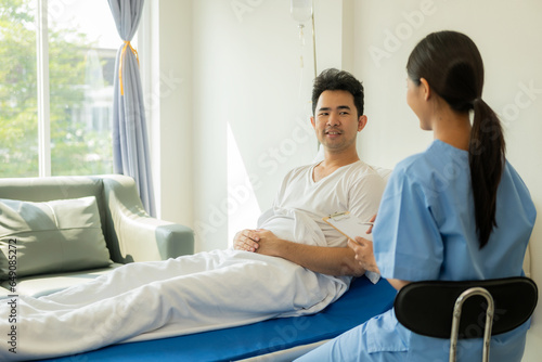 Asian male patient lies in bed while doctor examines and inquires about illness, female nurse writes health checklist at concept hospital Health insurance and hospital services