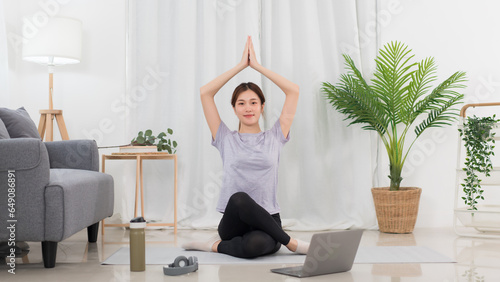 Yoga exercise concept, Asian woman raising arms over head in lotus position while doing yoga online