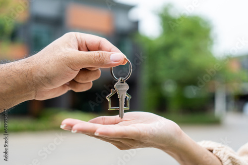 Woman buying or rent new home she holding key front of new house. Surprise happy young asian woman giving house key and smile to rent or purchase apartment home. Moving relocation concept.