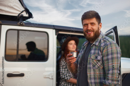 Portrait of hipster man traveler on background of car with tent on roof and mountains.