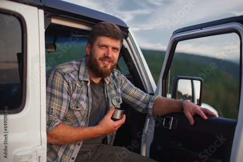 Portrait of hipster man traveler on background of car with tent on roof and mountains. © horimono