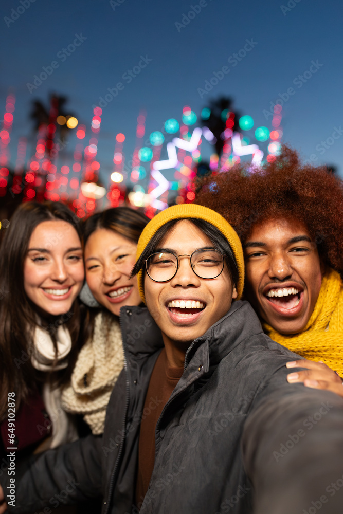 Multiracial friends having fun together taking vertical selfie during winter market at night looking at camera. Multiracial friends having fun together taking vertical selfie during winter market at night looking at camera.