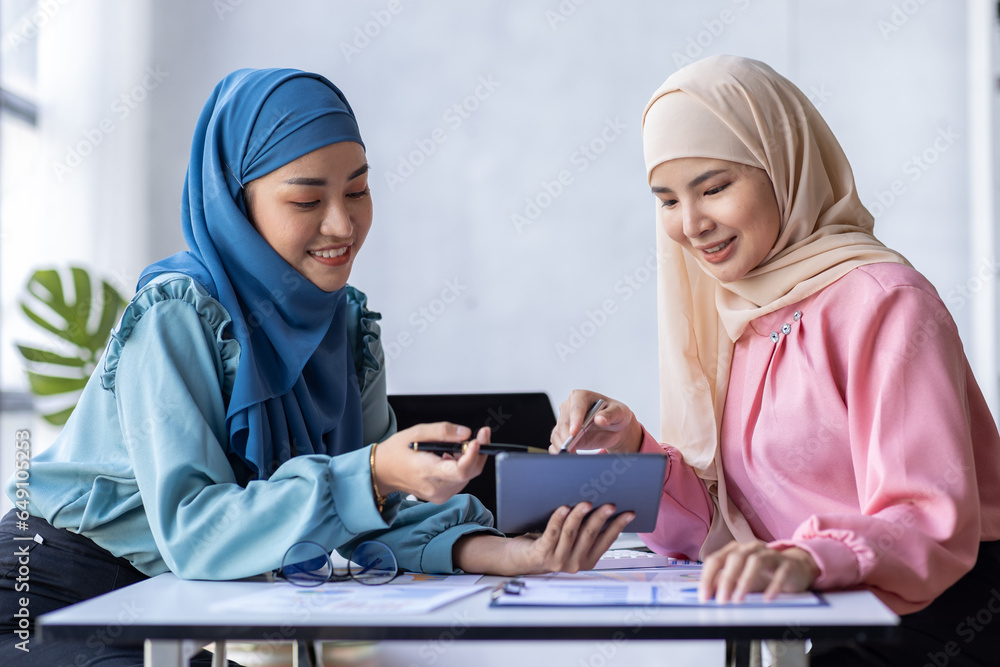 Two Young muslim business women point to graphs and charts to analyze market data, balance sheet, account, net profit to plan new sales strategies to increase production capacity. Two Young muslim business women point to graphs and charts to analyze market data, balance sheet, account, net profit to plan new sales strategies to increase production capacity.