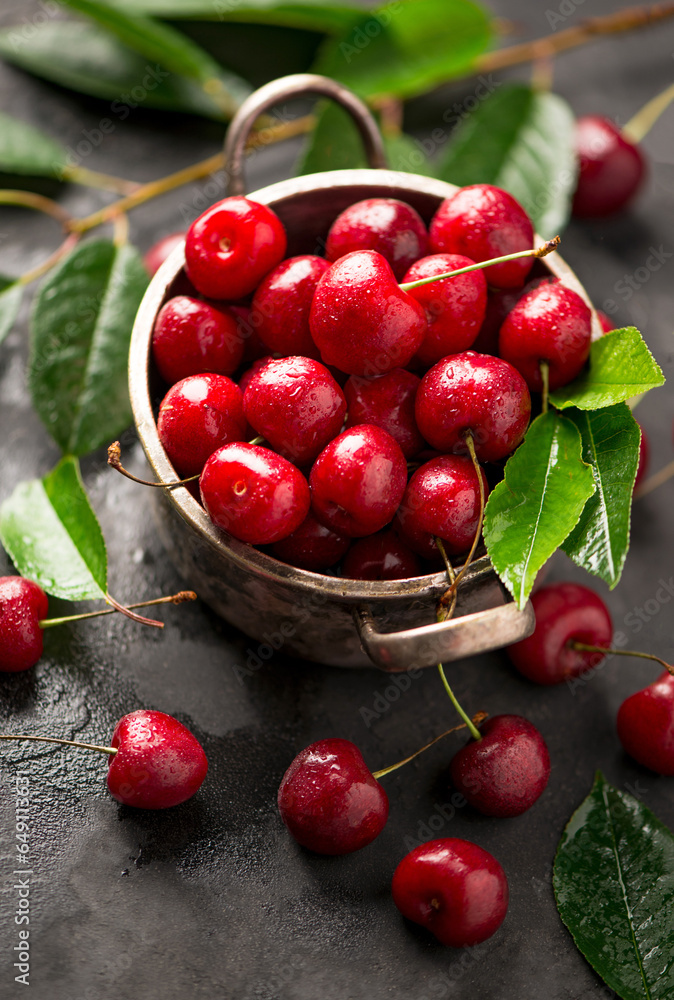 Seasonal harvesting of berries and fruits for the winter. Cherry jam. Cherry summer background. A large number of cherries with leaves on the table in a saucepan on a black background. close-up. Seasonal harvesting of berries and fruits for the winter. Cherry jam. Cherry summer background. A large number of cherries with leaves on the table in a saucepan on a black background. close-up.