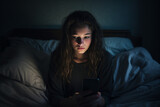 Dramatic Portrait of Single sad teen holding a mobile phone lamenting sitting on the bed in her bedroom with a dark light in the background