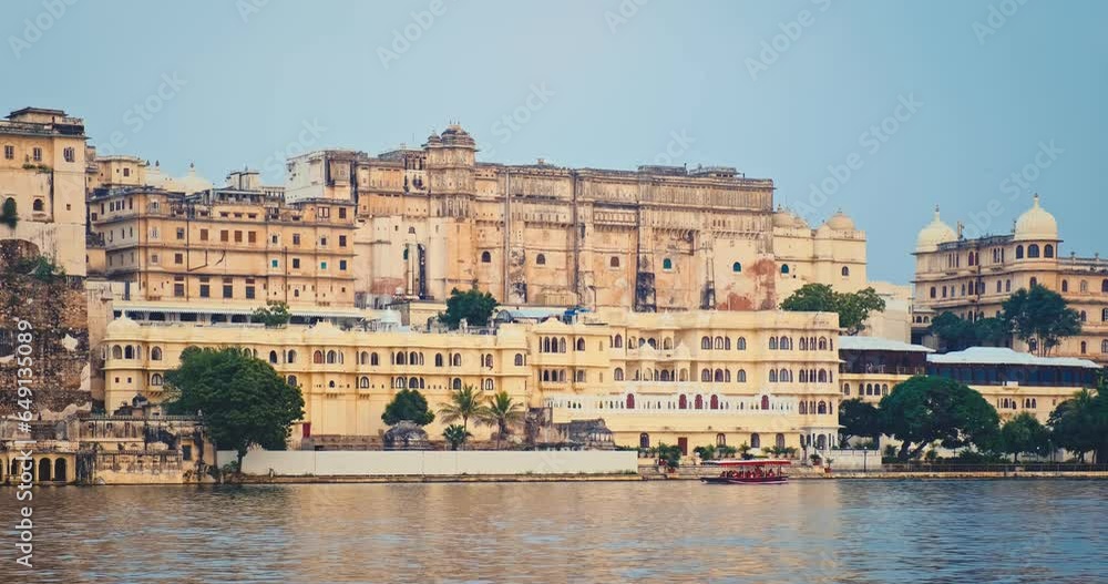 Udaipur City Palace view from lake Pichola on sunset with passing tourist boat. Jag Niwas is an example of Rajput architecture. Rajasthan is popular tourist Indian landmark. Incredible India heritage