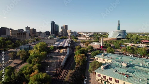 Aerial of Via Rail train entering Union Station in Winnipeg, MB. Human Rights Museum and Forks Market visible, 4K drone shot photo