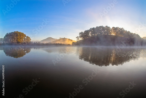 Dawn at the Golden Valley tourist area, the sun shines through the pine hills, shining rays of light on the surface of Suoi Vang lake
