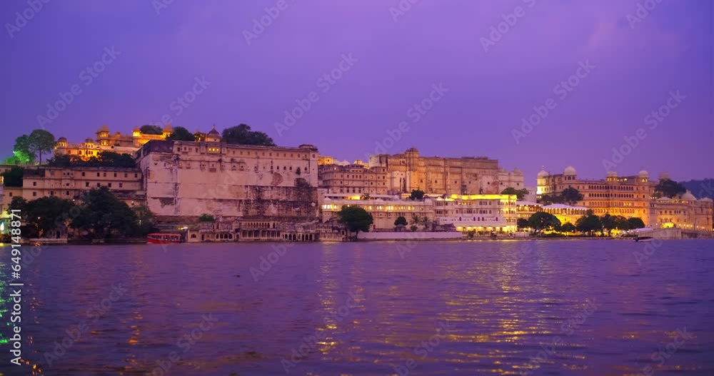 Famous tourism place Udaipur City Palace on bank Pichola lake illuminated on sunset with tourist boat, Rajput architecture of Mewars. Udaipur, Rajasthan, India, Asia Famous tourism place Udaipur City Palace on bank Pichola lake illuminated on sunset with tourist boat, Rajput architecture of Mewars. Udaipur, Rajasthan, India, Asia