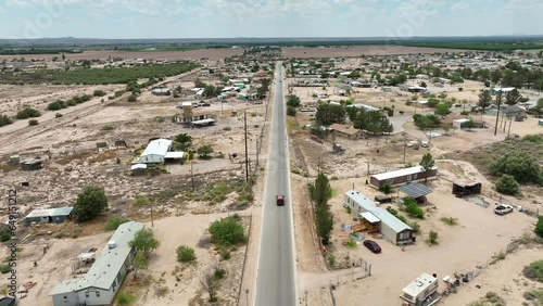 Truck driving through low income housing in Southwest USA desert. Small street surrounded by mobile home trailers on sandy plots of land.