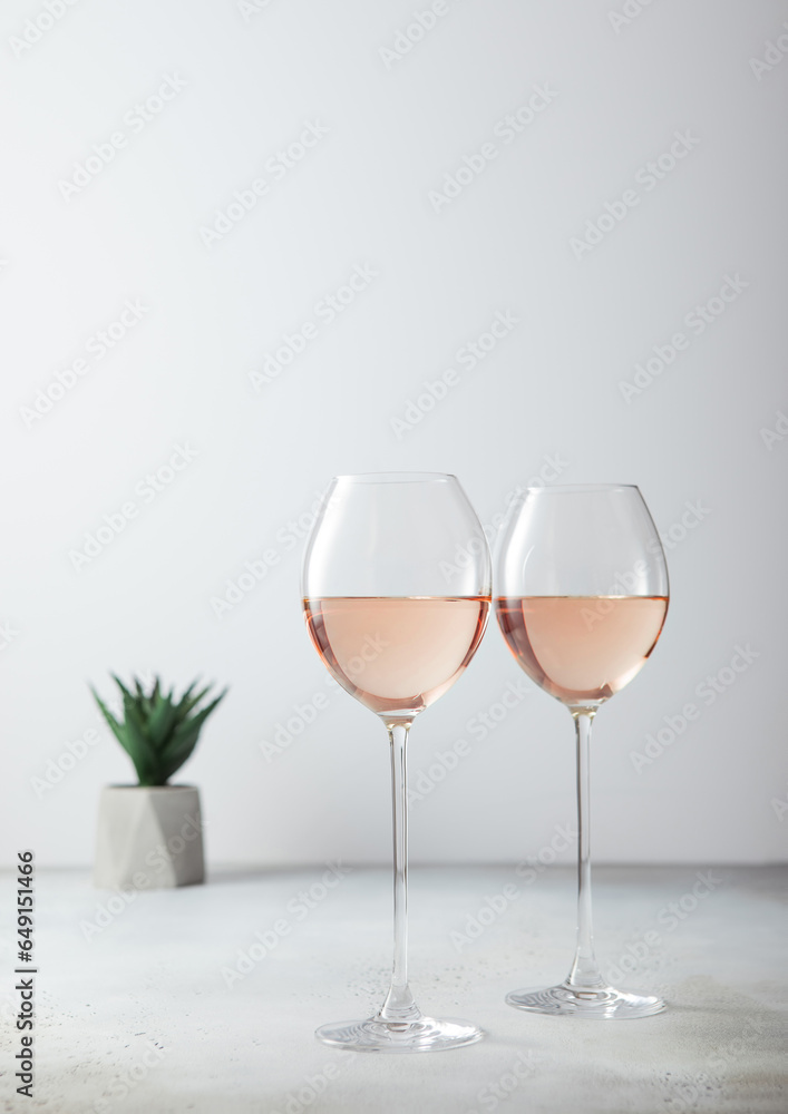 Fototapeta premium Pink rose glasses of wine with green plant on light background.