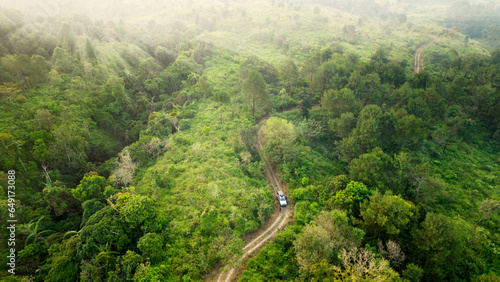 Valokuva Adventure morning road trip in the forest, aerial view of a 4x4 car on deep jung