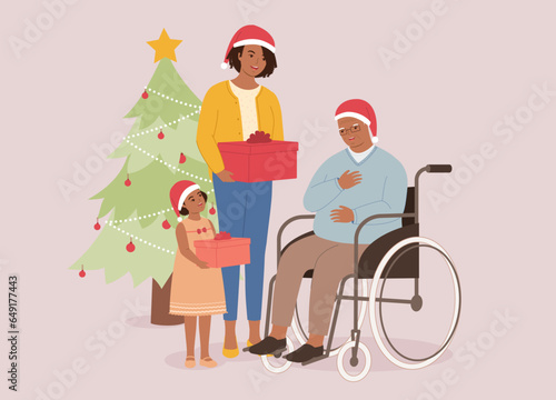 Smiling Black Mother And Her Little Daughter With Santa Hat Giving Christmas Present To Disabled Grandpa With Wheelchair. Full Length.