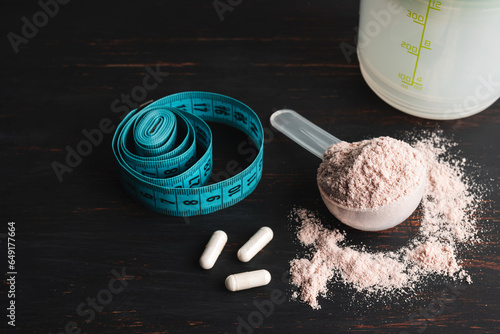 Scoop of chocolate whey protein isolate, white capsules of amino acids, creatine and measuring tape, bodybuilding food supplements on a dark wooden board photo