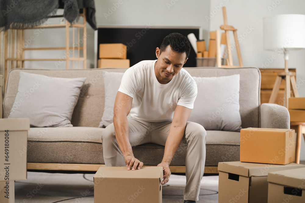 Young man carrying packed cardboard boxes with personal belongings to unfurnished cozy living room during move-in relocation day to new apartment. Young man carrying packed cardboard boxes with personal belongings to unfurnished cozy living room during move-in relocation day to new apartment.