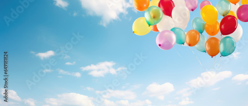 A large bunch of yellow Helium ballons straining on their strings against a sunny sky with white clouds
