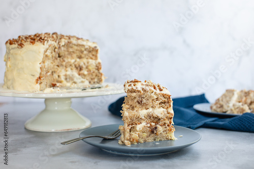 Three tier hummingbird or carrot cake with cream cheese frosting and pecan nuts or walnuts on a white cake stand with a slice being served on a plate