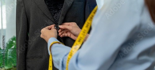 Close-up of tailoring a tailored suit on a male model, hand with tape measure, pin fastening jacket on male model.
