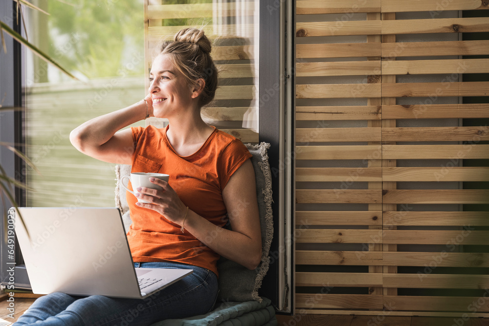 © Westend61 - Portrait of woman relaxing on balcony with laptop and mug