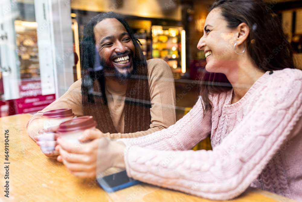 Happy multiracial couple sitting with coffee cups in cafe