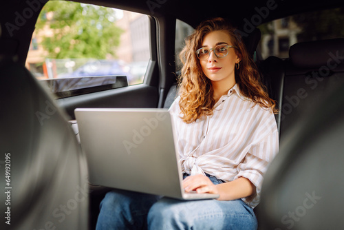 Stylish woman with laptop working in the back seat of a car. Work online. Business travel. Technology concept. © maxbelchenko