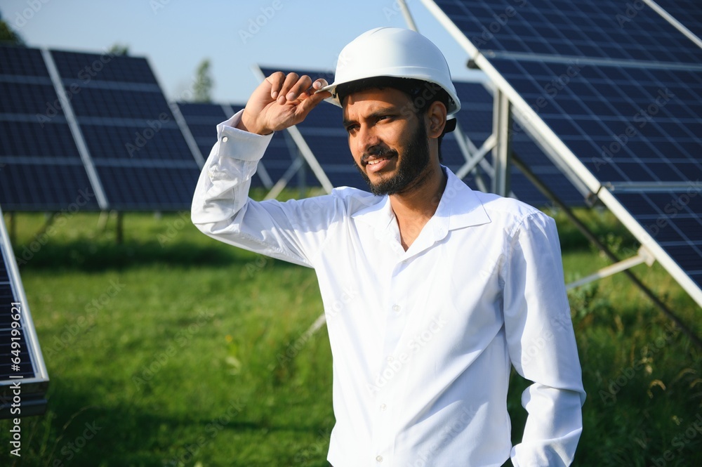 An Indian male engineer in a green vest is working on a field of solar panels. The concept of renewable energy. An Indian male engineer in a green vest is working on a field of solar panels. The concept of renewable energy.