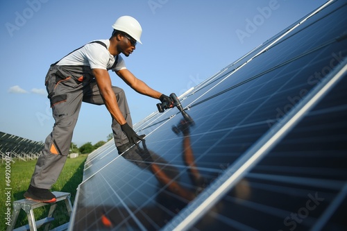 African American engineer maintaining solar cell panels. Technician working outdoor on ecological solar farm construction. Renewable clean energy technology concept
