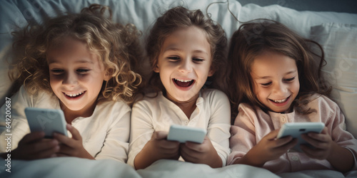 Happy smiling Children with smartphones lying in bed in the evening. Children and gadgets concept. 