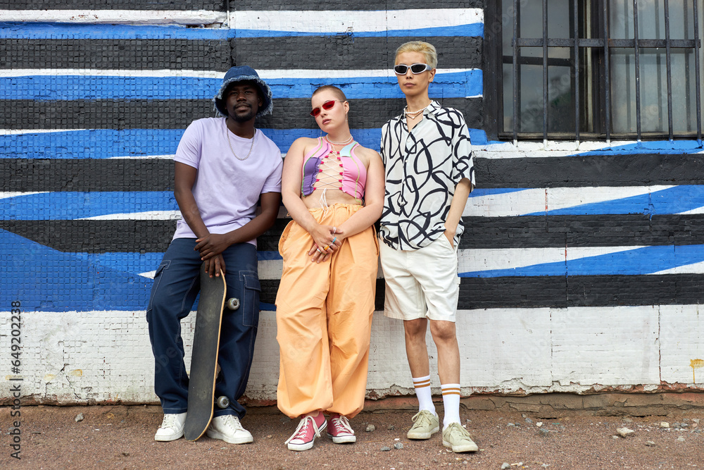 Full length portrait of multiethnic group of young people wearing trendy outfits posing against wall in urban setting, copy space