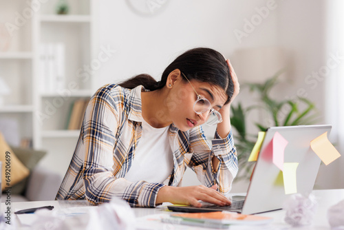 A tired young Indian girl gets angry from the number of tasks, crumples up the paper and throws it away, tries to calm down by meditating. Stressful work and study, overtasking. photo