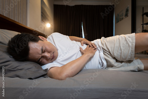 Sick asian middle aged man have a stomach aches,painful and discomfort,severe belly pain,Left-sided kidney infection or appendicitis,pain on left side of abdomen instead of the right,along with fever photo