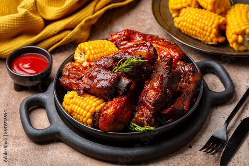 Food board with baked pork ribs with corn cobs, barbecue sauce, rosemary. Brown table background. Meat dinner. photo