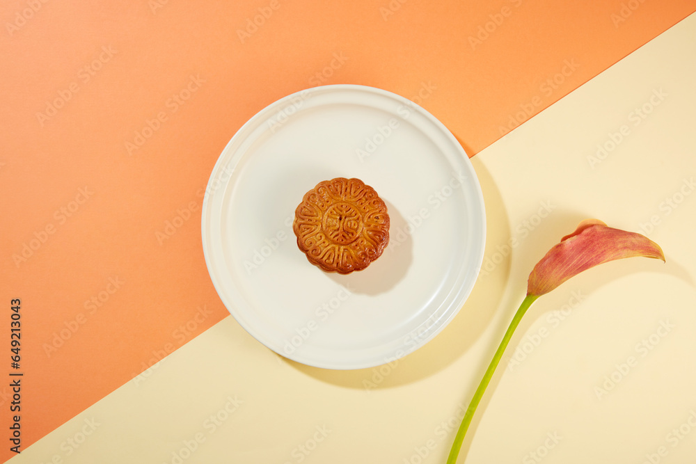 Minimal scene of a baked mooncake placed on white dish decorated with a branch of flower. Mid-Autumn Festival is a major holiday in Korea and China Minimal scene of a baked mooncake placed on white dish decorated with a branch of flower. Mid-Autumn Festival is a major holiday in Korea and China