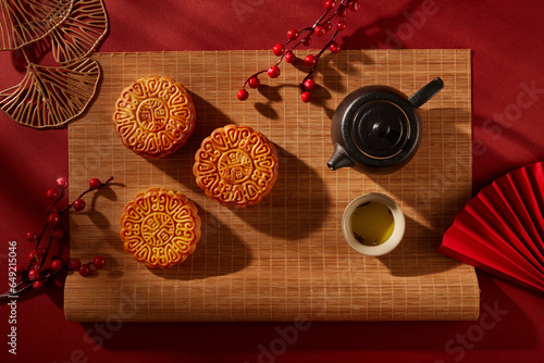 Bamboo blinds featured a tea set in black color and three mooncakes with elegant patterns. Tree branches decorated. Mid Autumn Festival minimalist design